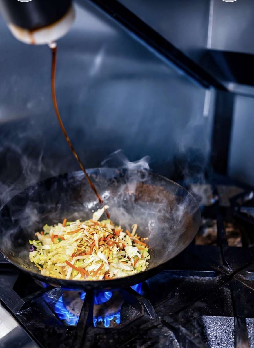 Vegetables cooking in a wok over a blue gas flame